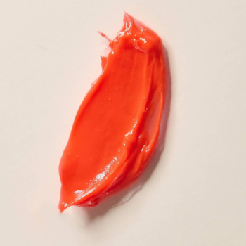 Zbliżenie na błyszczący, koralowy swatch peptydowego balsamu Say Hi Glassy Lips, rozmazany na beżowym tle.