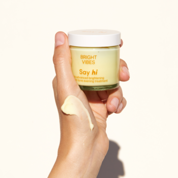 Ręka trzyma słoik żółtej kuracji rozjaśniającej Say Hi Bright Vibes; na dłoni widoczny swatch kremu.