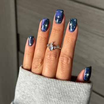 Lakier Semilac Virtual Blue: granatowe paznokcie z galaktycznym brokatem i fioletowym pyłem, dłoń z pierścionkiem.