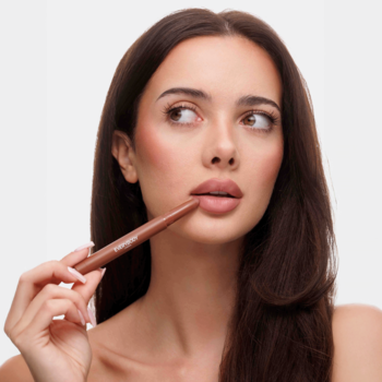 Kobieta z Blending Lip Crayon Bare Blush Everybody London przy ustach, brązowa, satynowa pomadka.