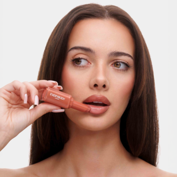 Plumping Lipstick Cinnamon Nude Everybody London, nawilżająca pomadka w brązowej tubce, przy ustach modelki.