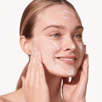 Zbliżenie na uśmiechniętą kobietę, która myje twarz delikatną mleczną emulsją MAKE IT CLEAR.