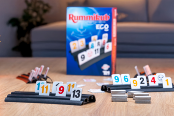 Rozłożona gra planszowa Rummikub Eco: tekturowe kostki, podstawki i pudełko na drewnianym stole.