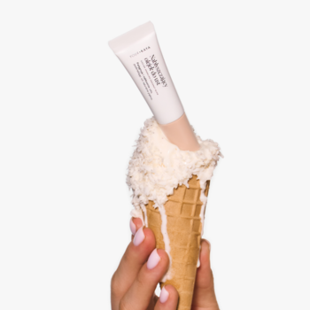 Nabłyszczający olejek do ust Sparkling Coconut Glow w tubce, zanurzony w rożku z topioną bitą śmietaną.