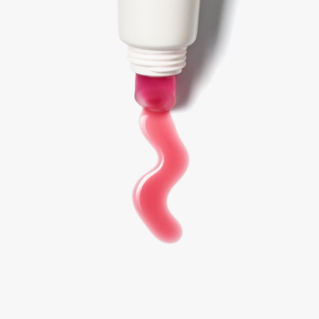 Różowy, błyszczący olejek do ust Hibiscus Glow wyciśnięty z białej tubki, tworzący falisty kształt.