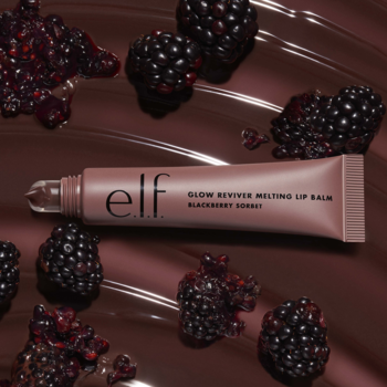 Nude tubka e.l.f. Glow Reviver Melting Lip Balm Blackberry Sorbet, leżąca wśród jagód na brązowym tle.