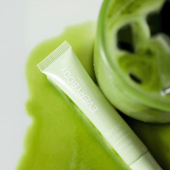 Tubka Everybody Peptide Lip Balm Matcha Latte leży na białym tle, otoczona rozlaną zieloną matchą.