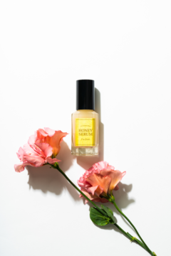 Koreańskie rozświetlające Honey Serum I'm From, żółta butelka z czarną nakrętką, obok dwa różowe kwiaty na bieli.