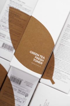Isntree Green Tea Fresh Toner, białe pudełko z brązowym liściem, widok na stos opakowań pod kątem.