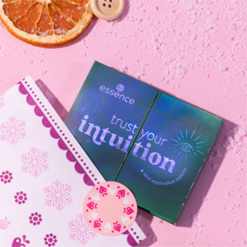 Mini paletka cieni Essence Trust Your Intuition, irydowa, na różowym pudrowym tle z notatnikiem i suszoną pomarańczą.