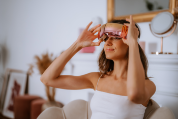 Masażer Beautifly OptiRelax Pro Smooth, kobieta w bieli zakłada różowo-złote urządzenie na oczy.
