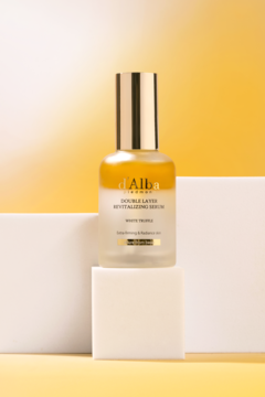 d'Alba White Truffle Serum dwuwarstwowe, złoto-żółte serum w matowej butelce na tle żółto-pomarańczowym.