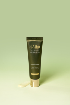 Oliwkowa tubka d'Alba Balancing Vegan Cream na zielonym tle, z wyciśniętą obok jasną kroplą kremu nawilżającego.