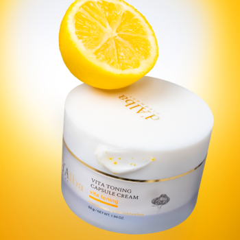 Kapsułkowy krem d'Alba Vita Toning, biały słoiczek z połówką cytryny na wieczku, na żółtym tle, od przodu.