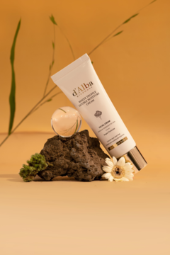 Biała tubka kremu d'Alba White Truffle Double Moisture Cream oparta o ciemny kamień, z kwiatem, na tle pomarańczowym.
