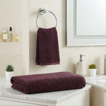 Dwa bordowe ręczniki frotte z prążkowaną fakturą w łazience; jeden złożony na blacie, drugi wisi na wieszaku.