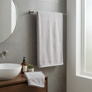 Szary ręcznik bawełniany z prążkowaną teksturą wisi na srebrnym wieszaku; złożony leży na drewnianej szafce w łazience.