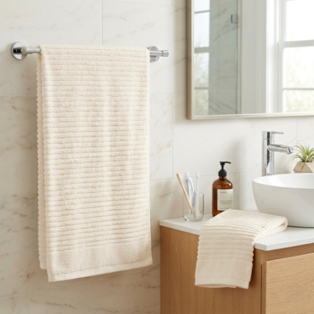 Kremowy, prążkowany ręcznik frotte wisi na relingu, a drugi złożony na drewnianej szafce w jasnej łazience.