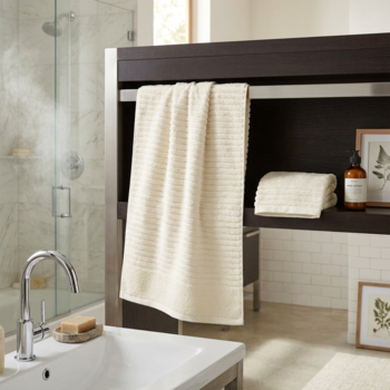 Kremowy, prążkowany ręcznik frotte wisi złożony na ciemnym wieszaku w eleganckiej łazience z wanną i prysznicem.