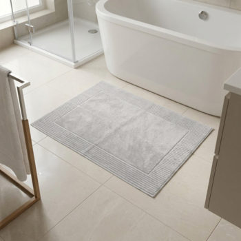 Jasnoszary dywanik łazienkowy 650gsm o prostokątnym kształcie i prążkowanej teksturze, na kafelkowej podłodze w łazience.