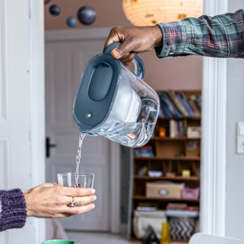 Zbliżenie na grafitowy dzbanek filtrujący BRITA Style Essential z LED, z którego nalewa się wodę do szklanki.