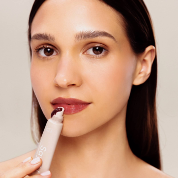 Kobieta aplikuje peptydowy balsam Say Hi Glassy Lips Berry na usta. Produkt w jasnej tubce, widoczny intensywny kolor.