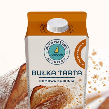 Bułka tarta Młyn Mazurki w białym kartonie z brązową górą i nakrętką, widok z przodu, na tle chleba i okruszków.