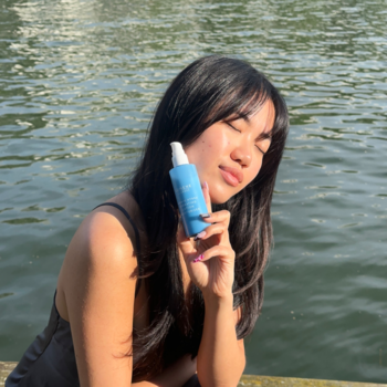 Kobieta z zamkniętymi oczami trzyma niebieski spray Lumene Nordic Hydra Lähde, lekki lotion nawilżający do twarzy.