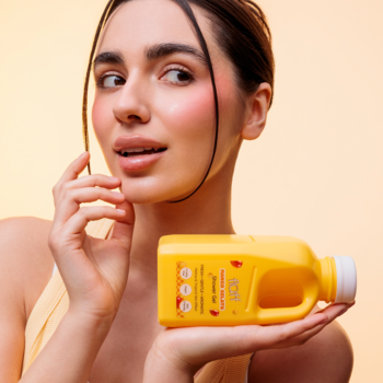 Kobieta trzyma poziomo żółtą butelkę Fluff Mango Gelato, żel pod prysznic o zapachu mango, i odwraca głowę.