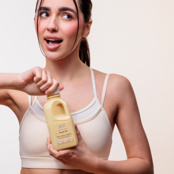 Kobieta otwiera jasną butelkę Fluff Butter Milk Żel pod prysznic, z mlecznym zapachem i ekstraktem z owsa.