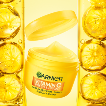 Garnier Vitamin C Fresh & Bright, rozświetlający krem-sorbet w żółtym słoiczku z uniesioną pokrywką, na tle cytrusów.