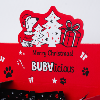 Czerwony kalendarz adwentowy dla psa, otwarty, z pop-upem: jamnik Mikołaj, choinki, napis 'Merry Christmas! BUBĄlicious'.