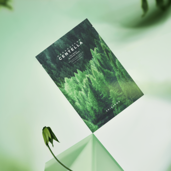 SKIN1004 Madagascar Centella Tea-Trica Relaxing Mask, zielona maska z lasem, pionowo na błyszczącej zielonej powierzchni.