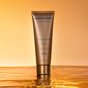Sensum Mare Algoglow rozświetlający balsam do ciała w złotej tubie, stojący na błyszczącej, wodnej tafli.