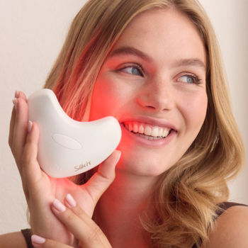 Silkn LumiLips: białe, ergonomiczne urządzenie LED emitujące czerwone światło na ustach uśmiechniętej kobiety.
