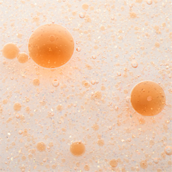 Makro zdjęcie Catrice Aura Drop Lip Elixir: pomarańczowe, błyszczące kropelki w jasnej emulsji.