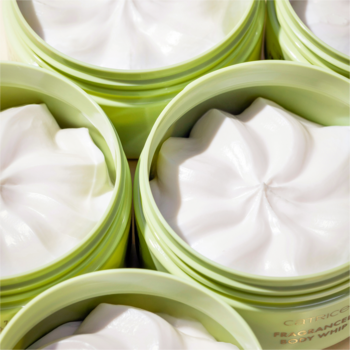 Zbliżenie na kilka otwartych, jasnozielonych słoików z białym, puszystym balsamem do ciała o wirującej teksturze.