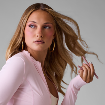 Kobieta z różowym makijażem i blond włosami trzyma jasnoróżową, wykręcaną konturówkę Everybody London Blush Icing.