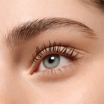 Zbliżenie na jasne, niebiesko-szare oko z wytuszowanymi rzęsami oraz naturalnie gęstymi, ciemnymi brwiami.