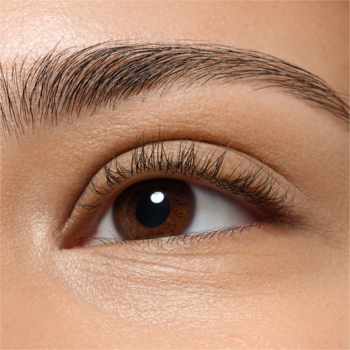 Zbliżenie na prawe, otwarte oko o brązowej tęczówce, z długimi rzęsami i ciemną brwią. Naturalny odcień skóry.