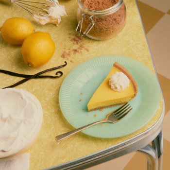 Perfumy Sweet Tooth Lemon Pie. Kawałek cytrynowego ciasta z kremem na zielonym talerzu, obok cytryny i wanilia.