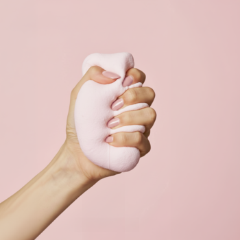 Dłoń ściska różowy, puszysty kształt na jasnym tle, nawiązujący do odżywki COOLNAILS Marshmallow Hardener.