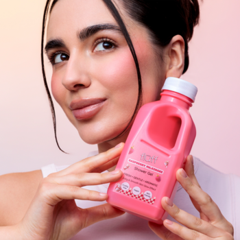 Kobieta trzyma różowy żel pod prysznic Fluff Raspberry Milkshake, butelkę z uchwytem o malinowym zapachu.