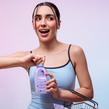 Kobieta otwiera fioletowy żel pod prysznic Fluff Blueberry Mochi, z radosnym wyrazem twarzy, obok koszyk.