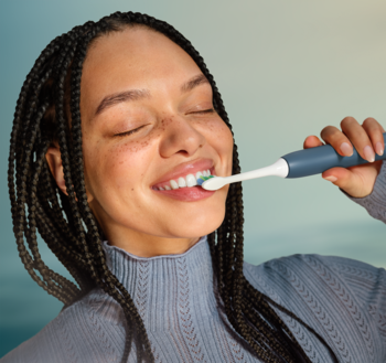 Szczęśliwa kobieta używa niebieskiej, sonicznej szczoteczki do zębów. Z bliska, polecanej przez dentystów.