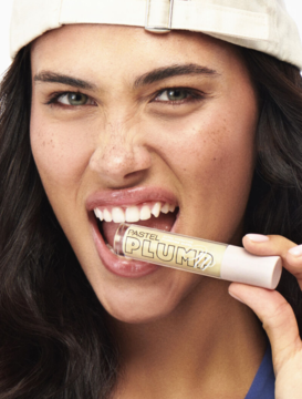 Kobieta z błyszczykiem Pastel Plump Up 201 Royal między zębami, dla ust z objętością i blaskiem.