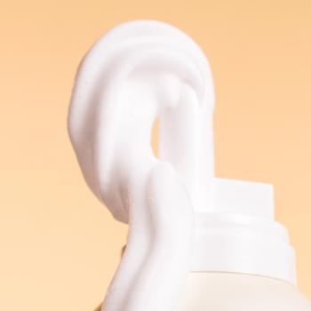 Zbliżenie na białą, puszystą pianę balsamu do ciała Butter Milk wydobywającą się z białego dozownika.