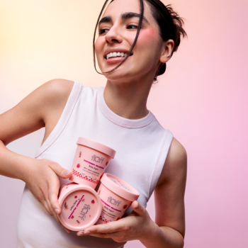 Uśmiechnięta kobieta prezentuje 3 różowe słoiczki Fluff Raspberry Milkshake Body Yogurt, lekkiego balsamu.