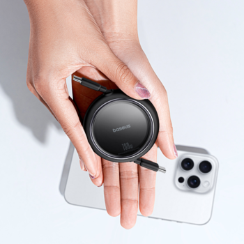 Ręka trzyma czarny, okrągły Baseus Free2Draw Mini, wysuwany kabel USB-C na tle białego iPhone'a.
