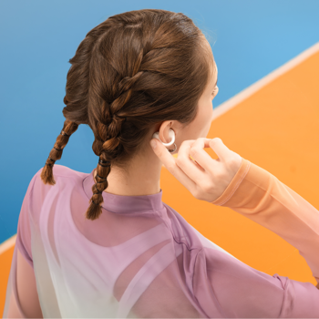 Białe słuchawki Baseus Bass BC1 Open-Ear, clip-on, na uchu kobiety z warkoczami. Widok z tyłu, sportowe tło.